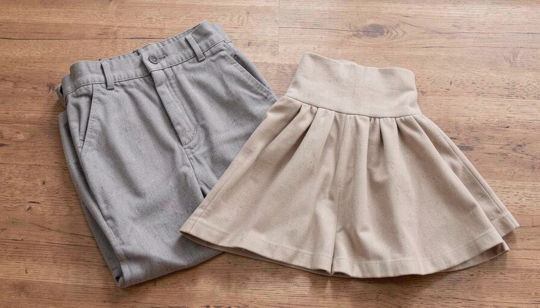 A pair of tailored shorts and a flared mini skirt in neutral tones, folded neatly on a wooden surface